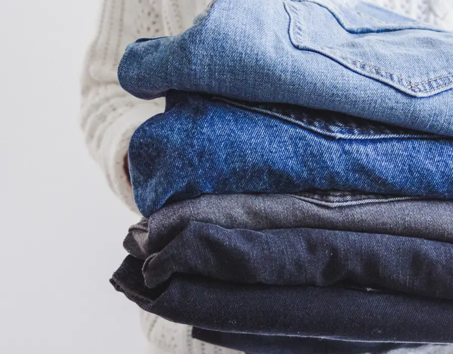 Persona entregando una pila de jeans doblados